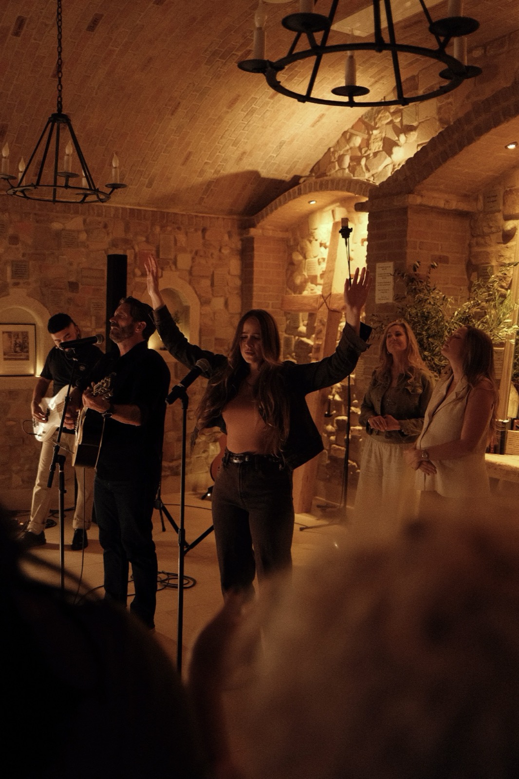 Worshippers with hands raised beneath chandeliers during evening worship at The Hidden Encounter