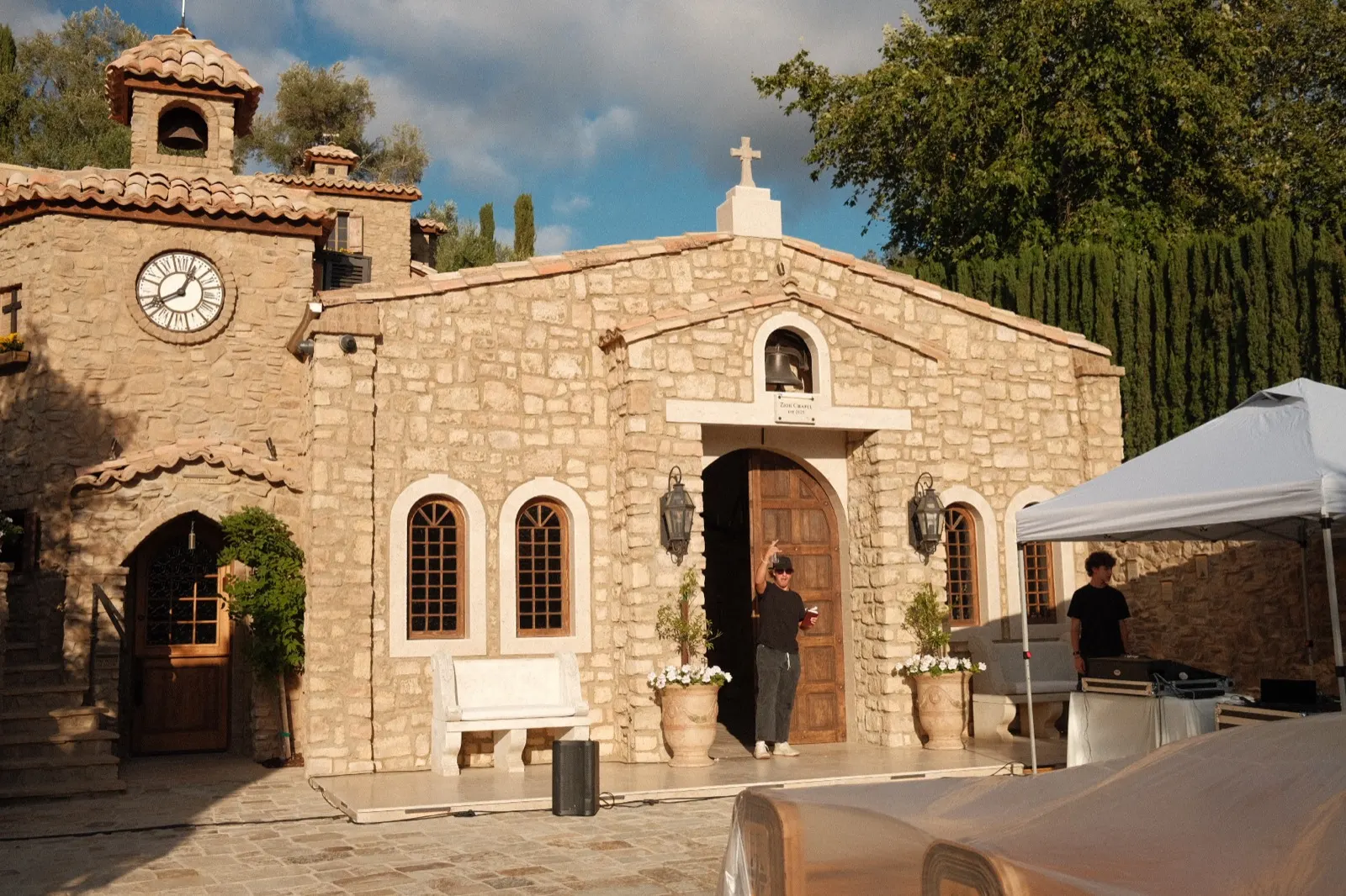 The stone chapel at golden hour, clock tower and cross above the entrance, set for a worship gathering