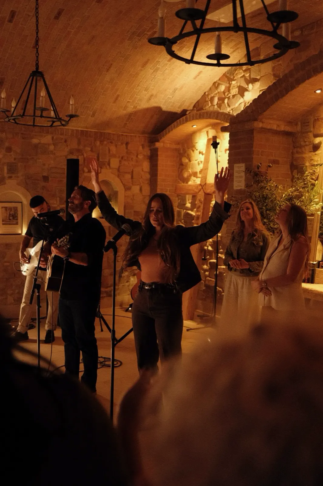 Worshippers with hands raised beneath chandeliers during evening worship at The Hidden Encounter
