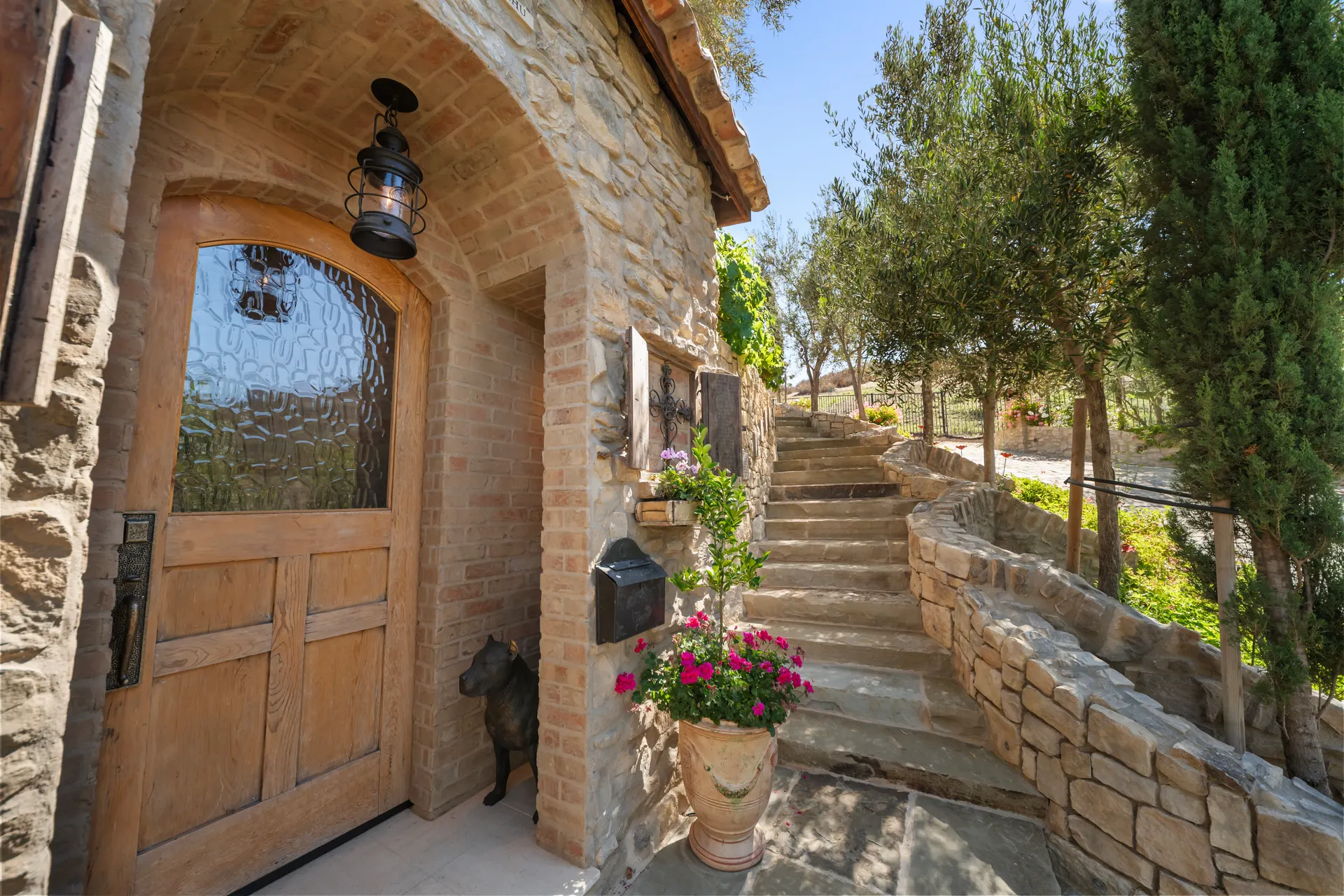 Arched wooden door beneath a brick vault, iron lantern lit above it, stone stair climbing past