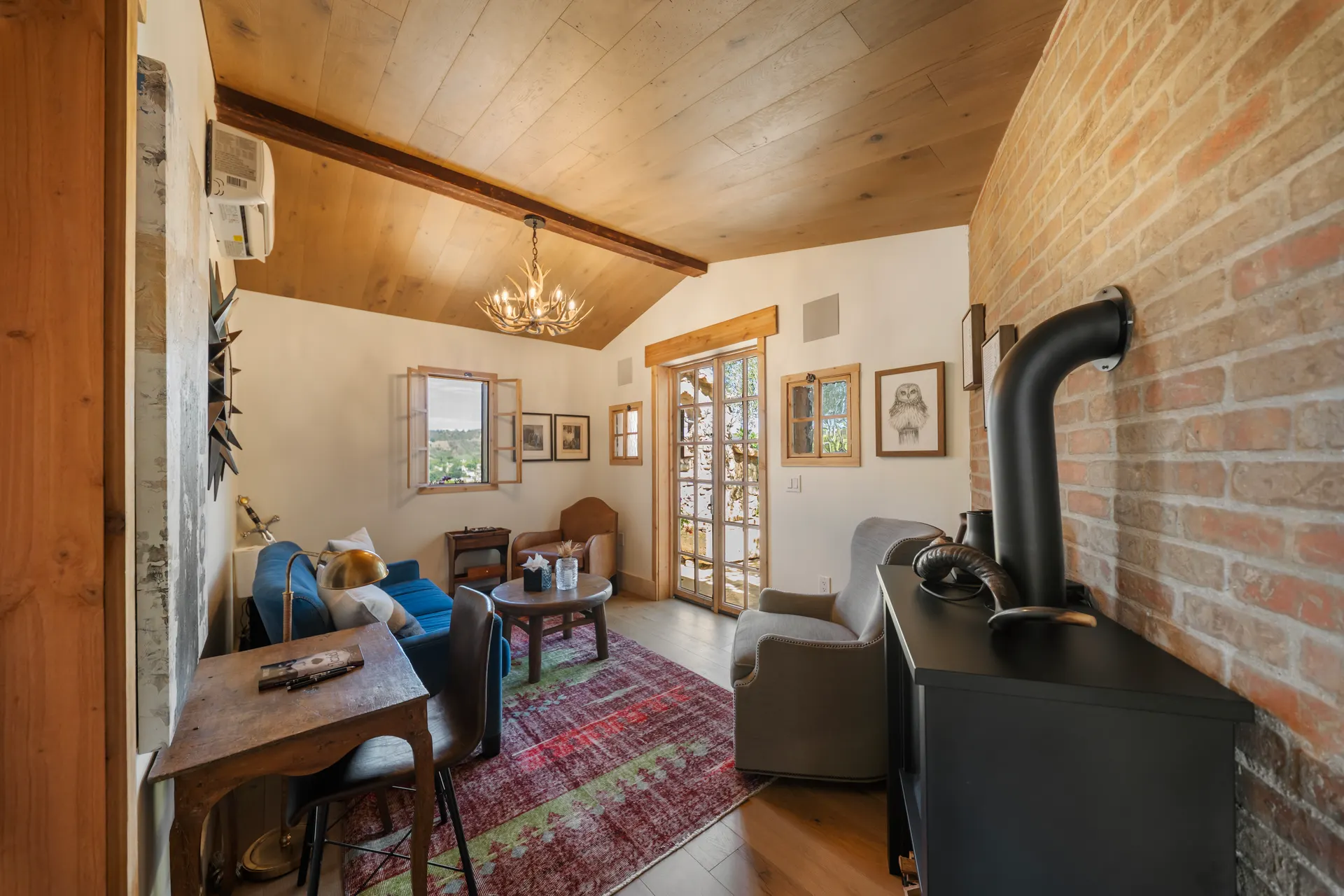 Sitting room with a plank ceiling, exposed brick wall, blue sofa, wood stove and a red kilim rug