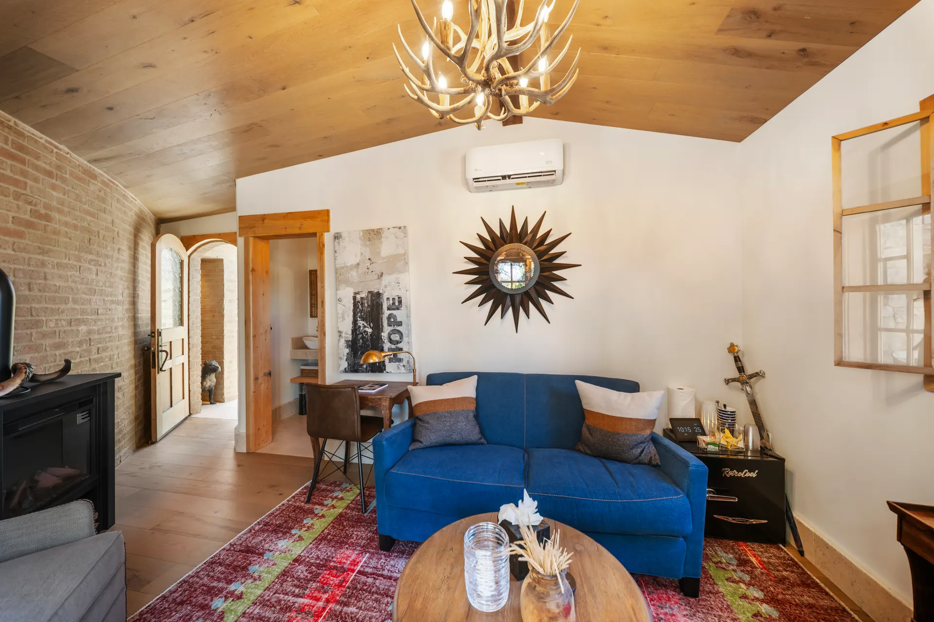 Blue sofa beneath a sunburst mirror, kilim rug, doorway leading through to the bath