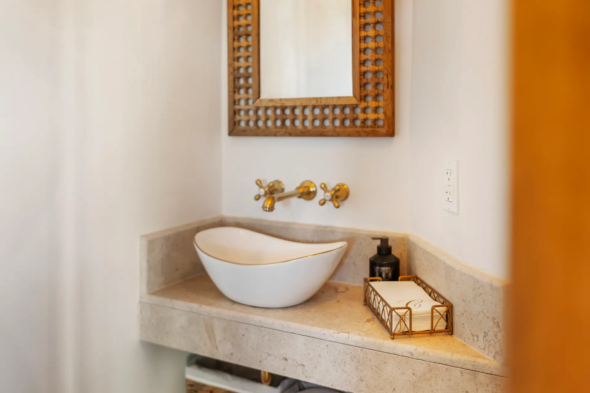 Carved stone basin on a travertine counter with brass wall taps