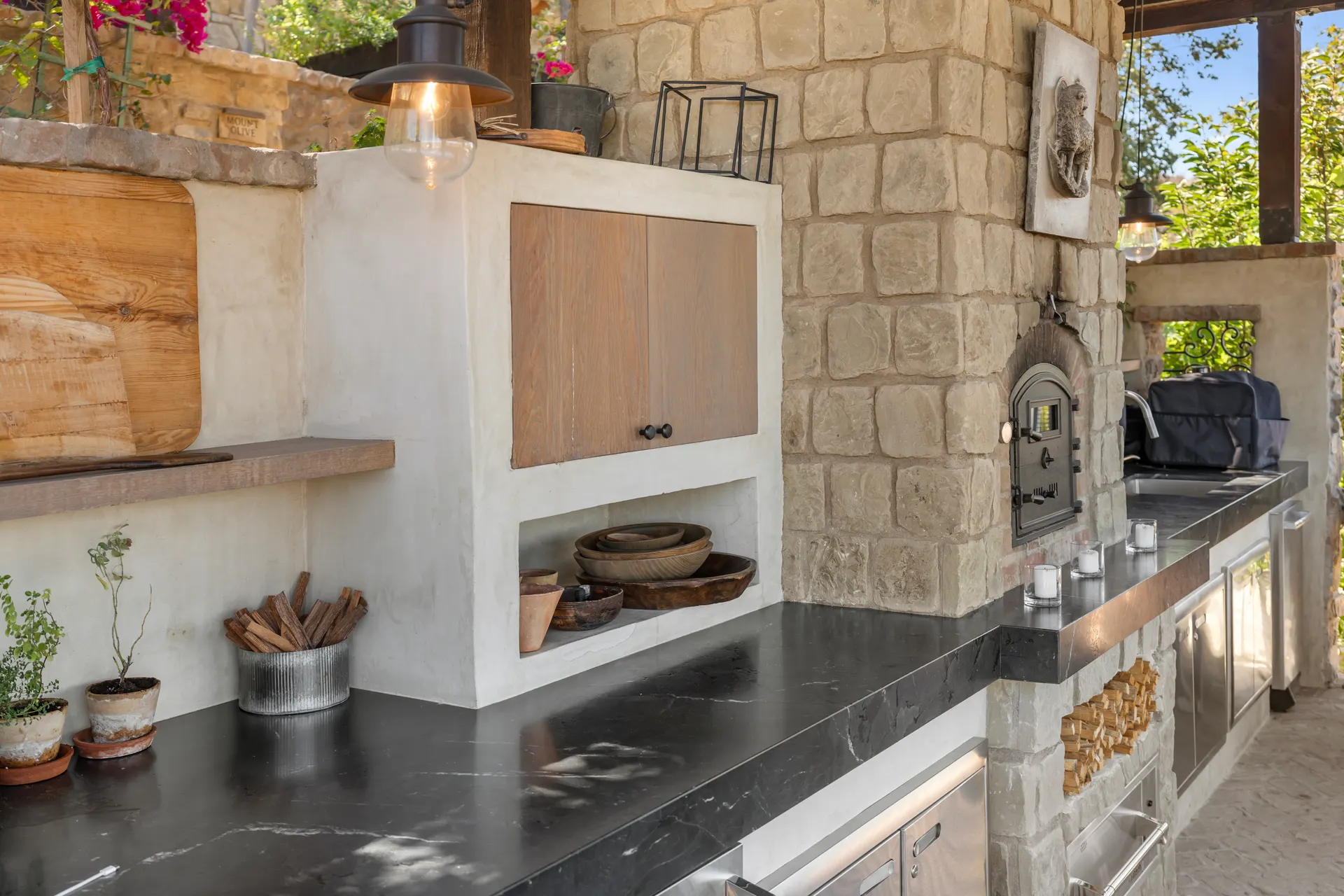 Counter and hearth beneath the pavilion roof, timber shelving and stone surround
