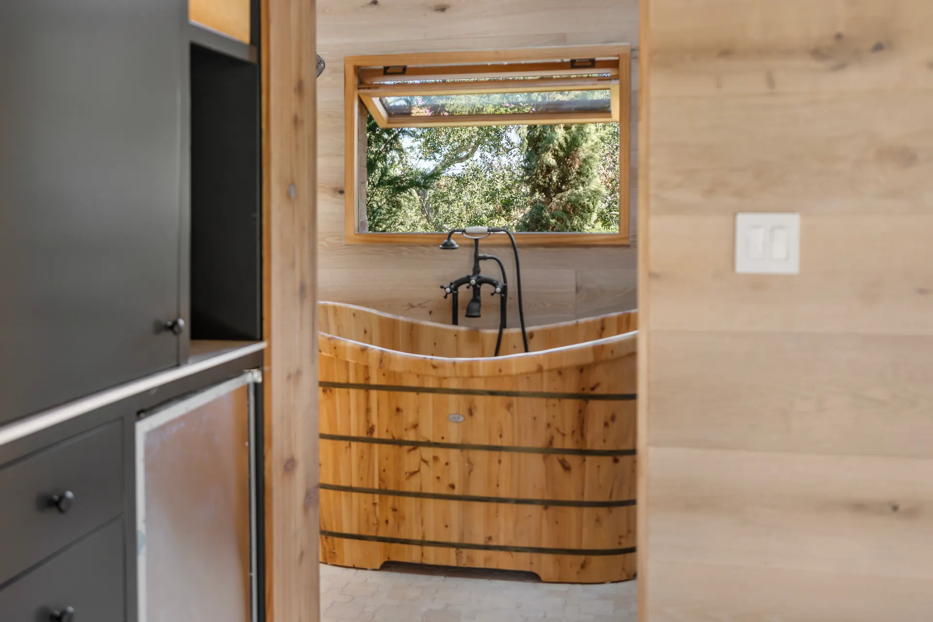 Wooden soaking tub with iron fittings, cabinetry and plank wall