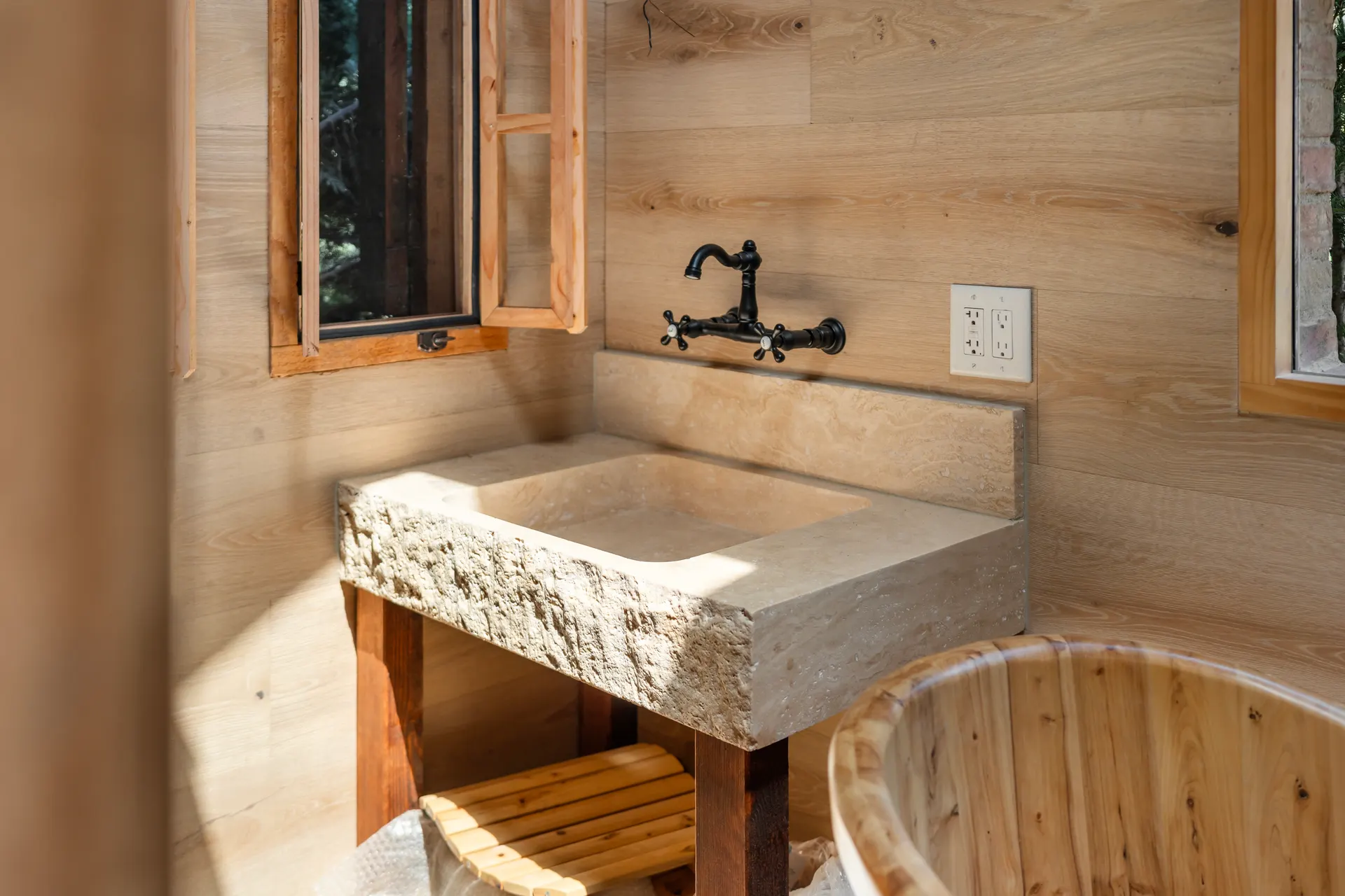Carved stone trough basin on a timber stand beside a wooden soaking tub