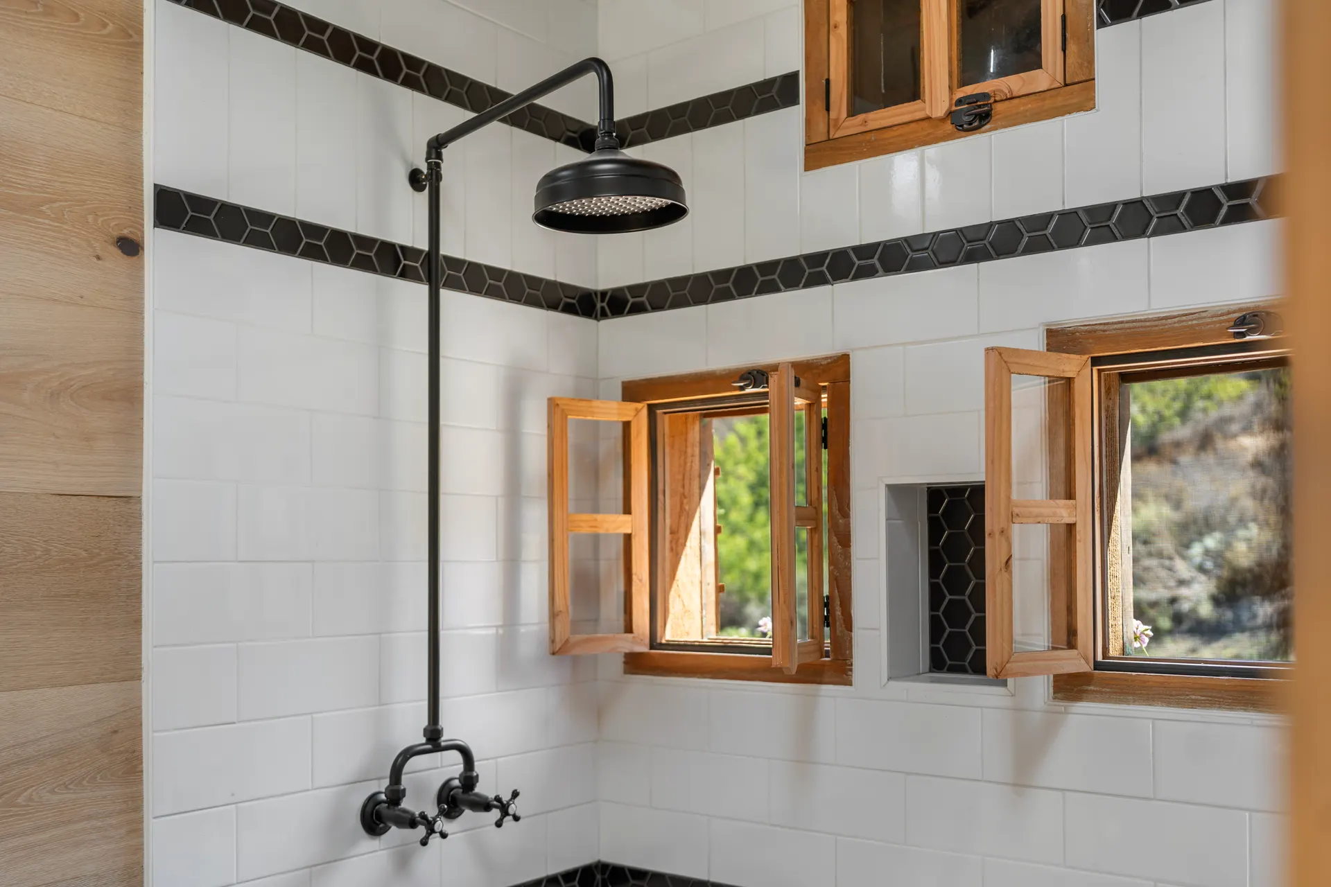 Shower lined in white tile with a black rain head and shuttered timber windows