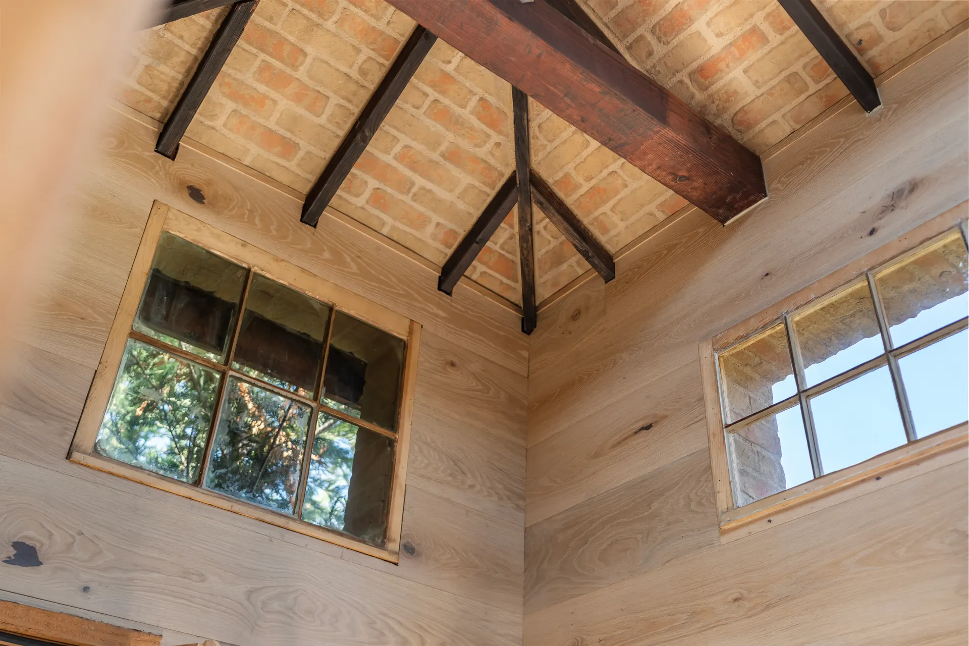 Empty room with plank walls, dark timber roof trusses and two shuttered windows