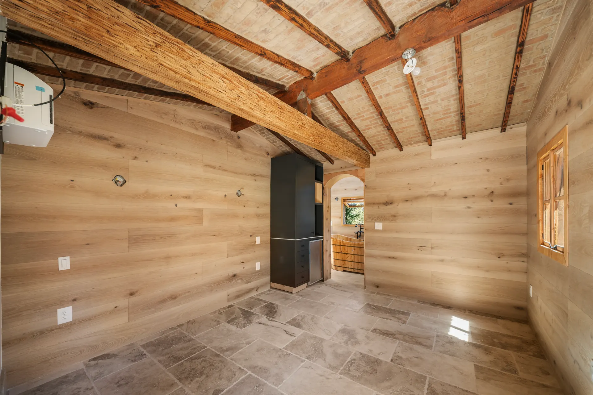 Empty room with plank walls, timber trusses overhead and a stone tile floor