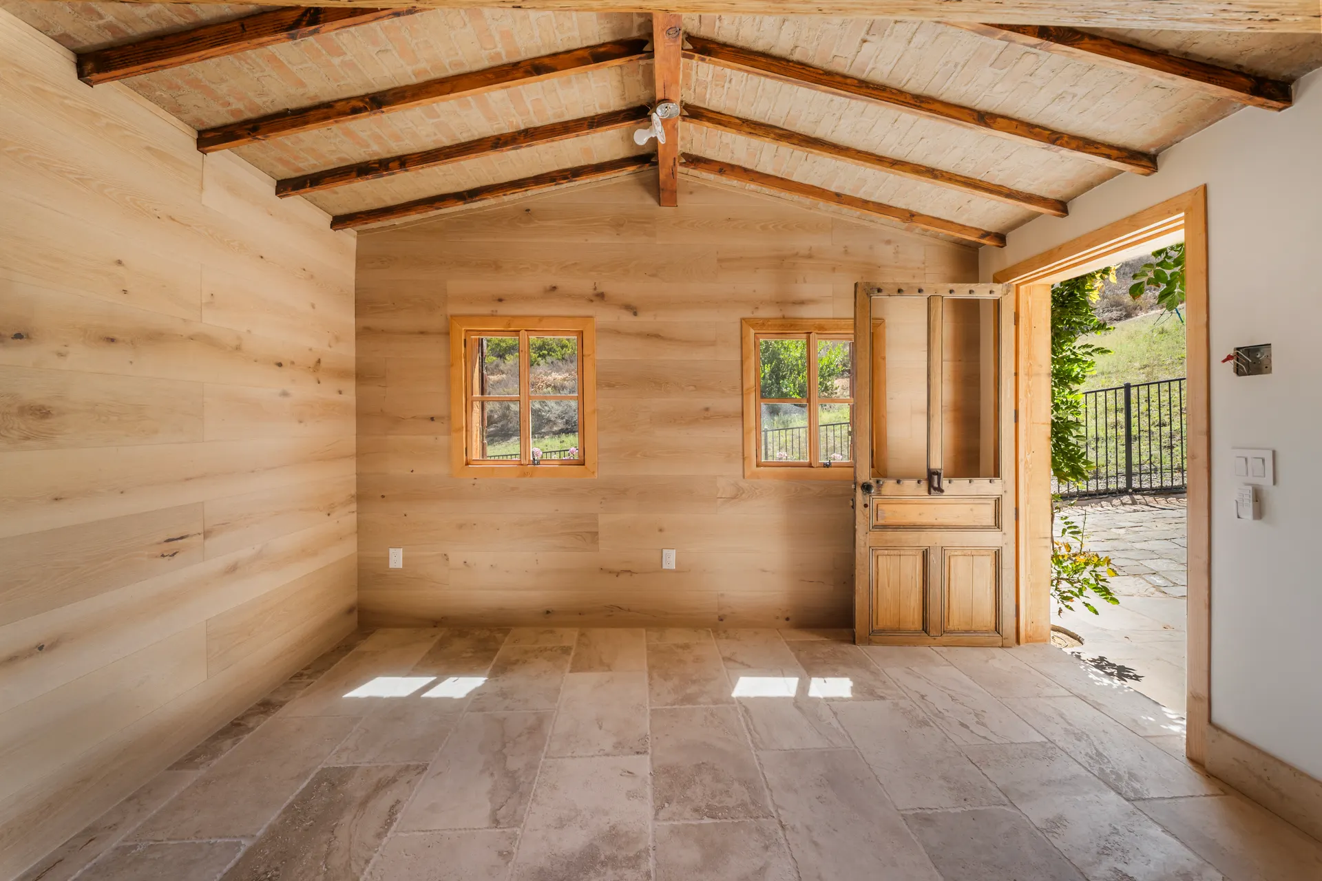 Empty room with plank walls and a door standing open to the daylight outside