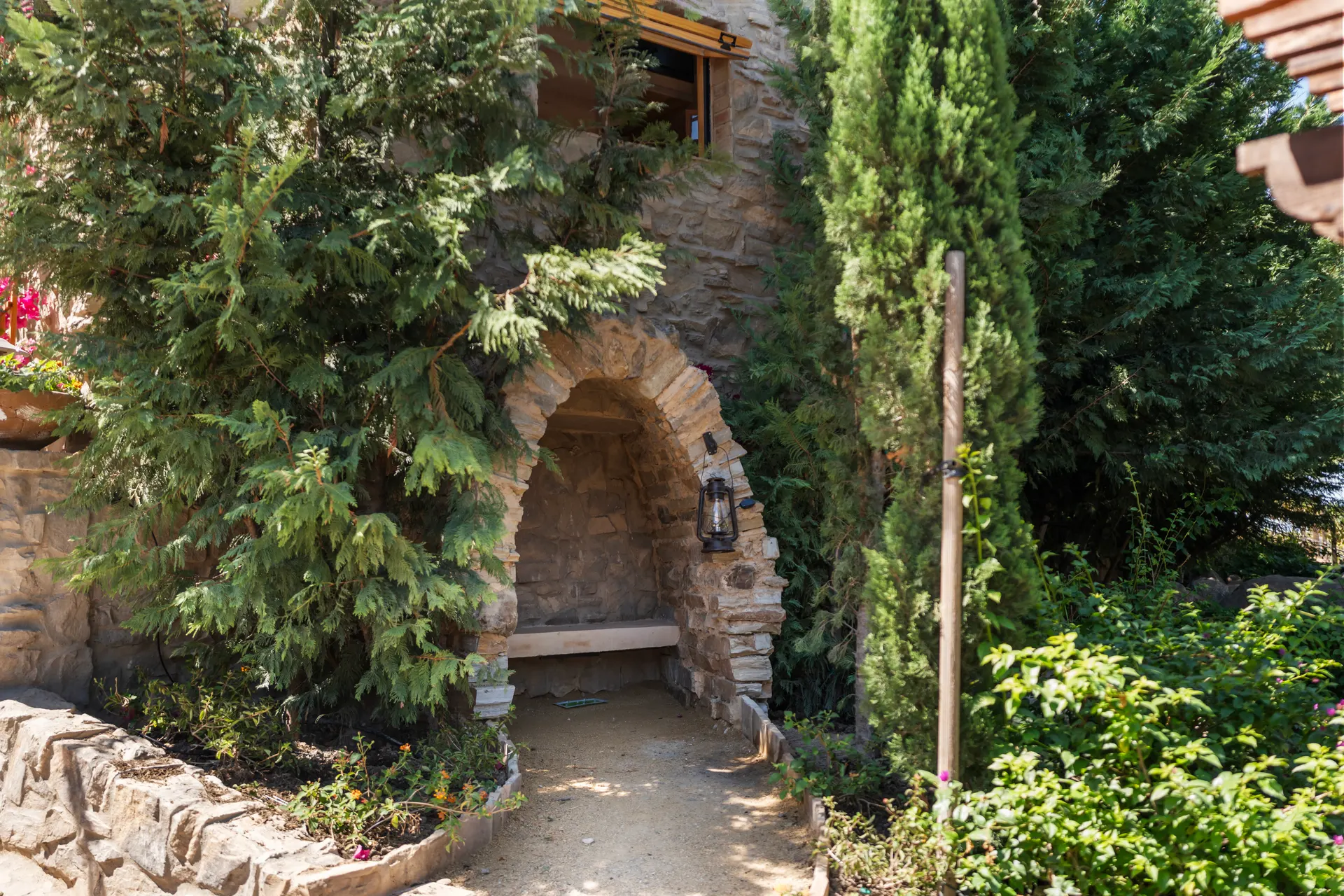 Stone grotto arch with a bench set inside it, cypress and planting either side