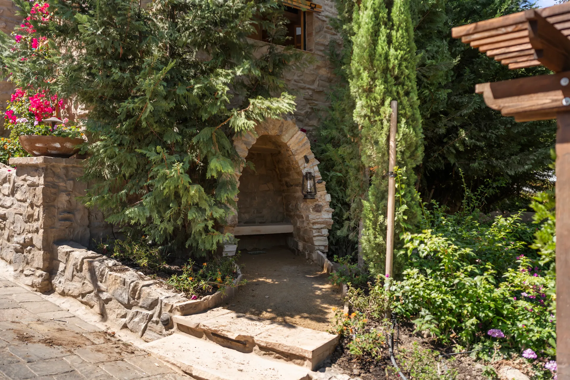 Stone grotto arch and bench seen across the planting, lantern hung inside