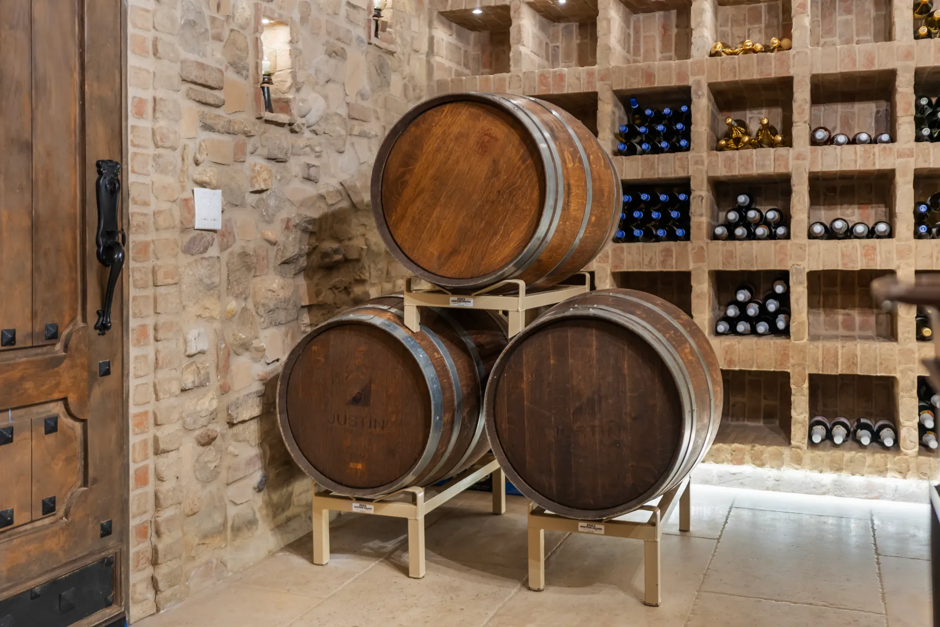 Oak barrels stacked on a stand against a wall of racked bottles