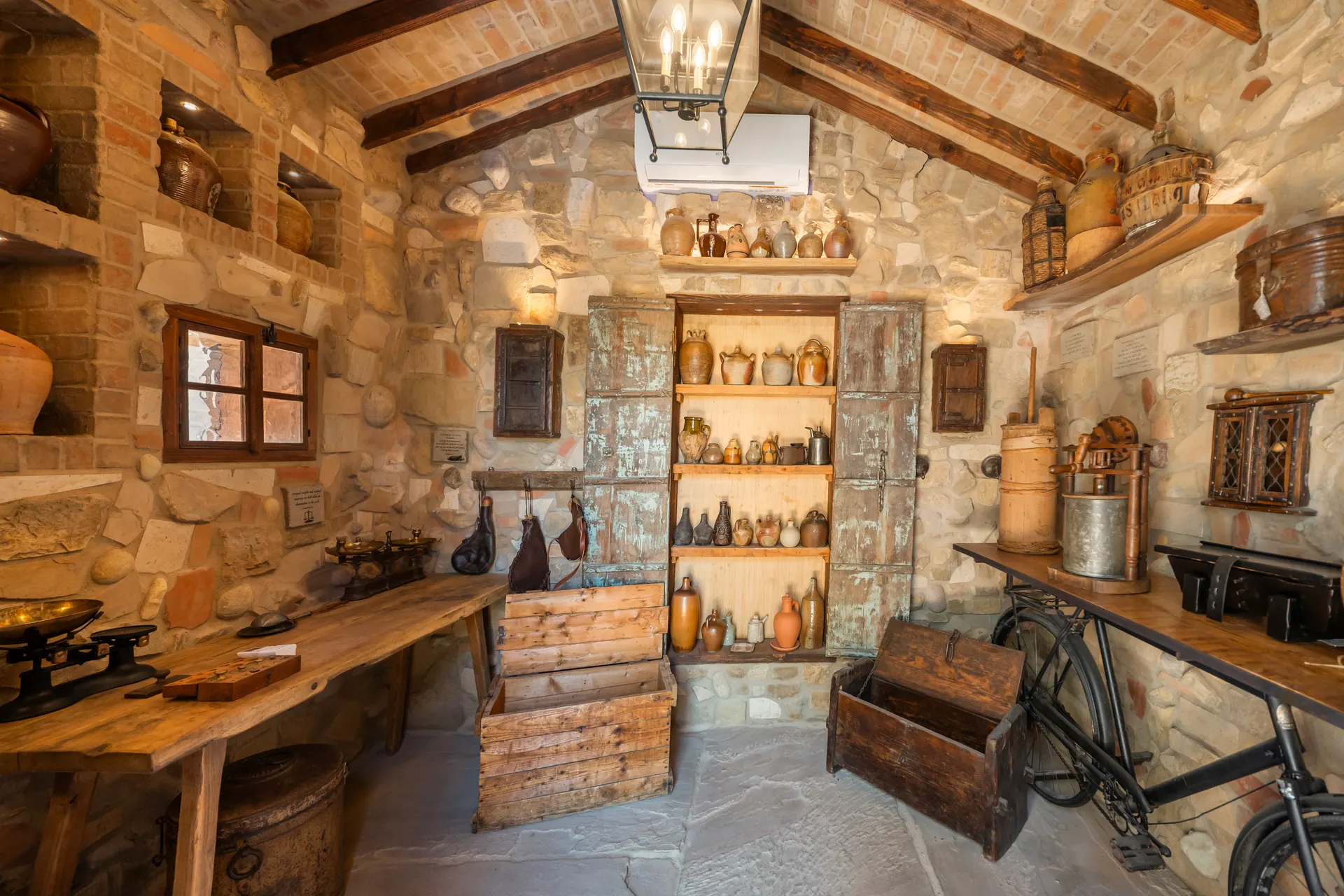Cellar room lined with clay vessels and scales, a timber work table at the centre