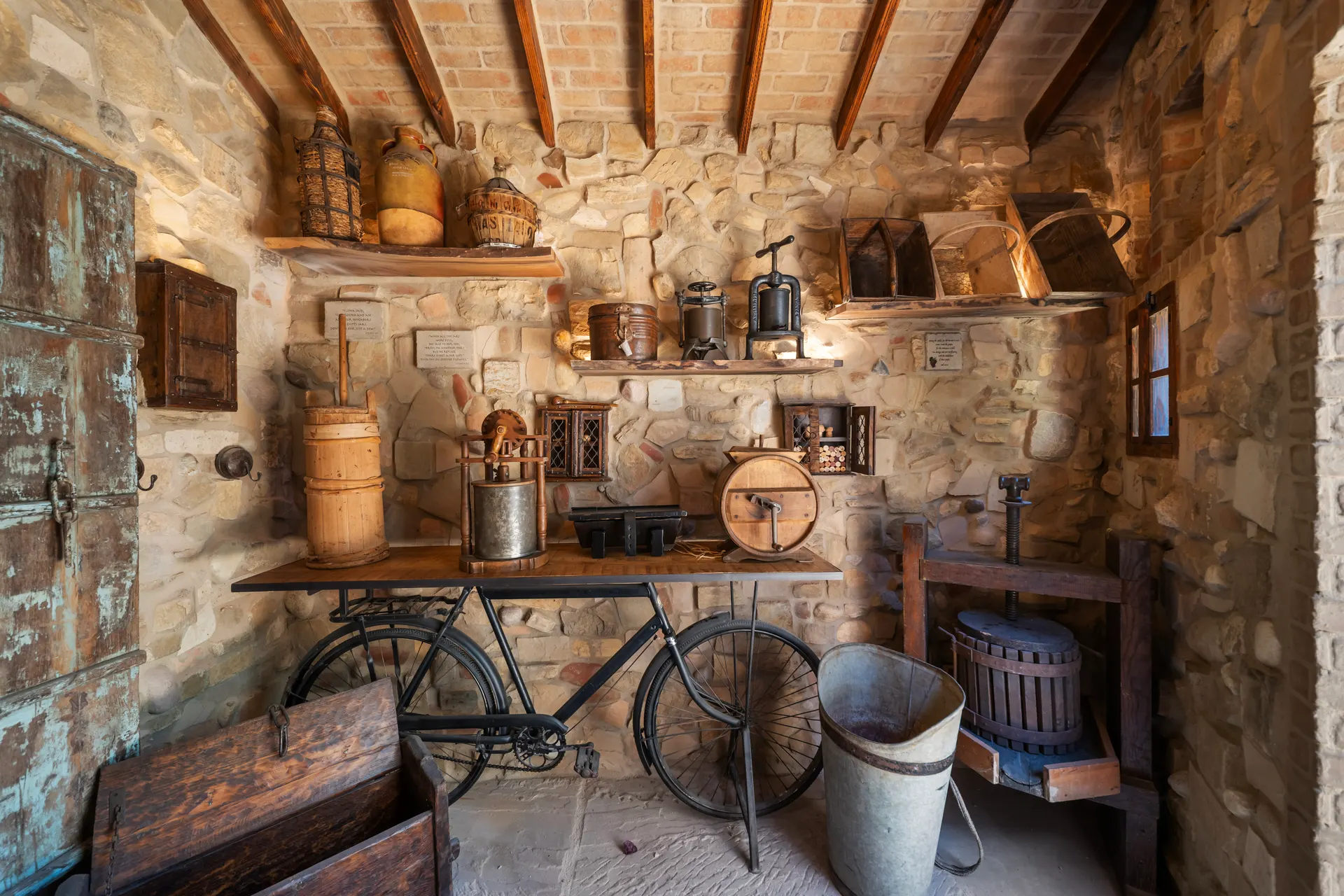 Vintage bicycle and a fruit press standing against a stone wall hung with vessels