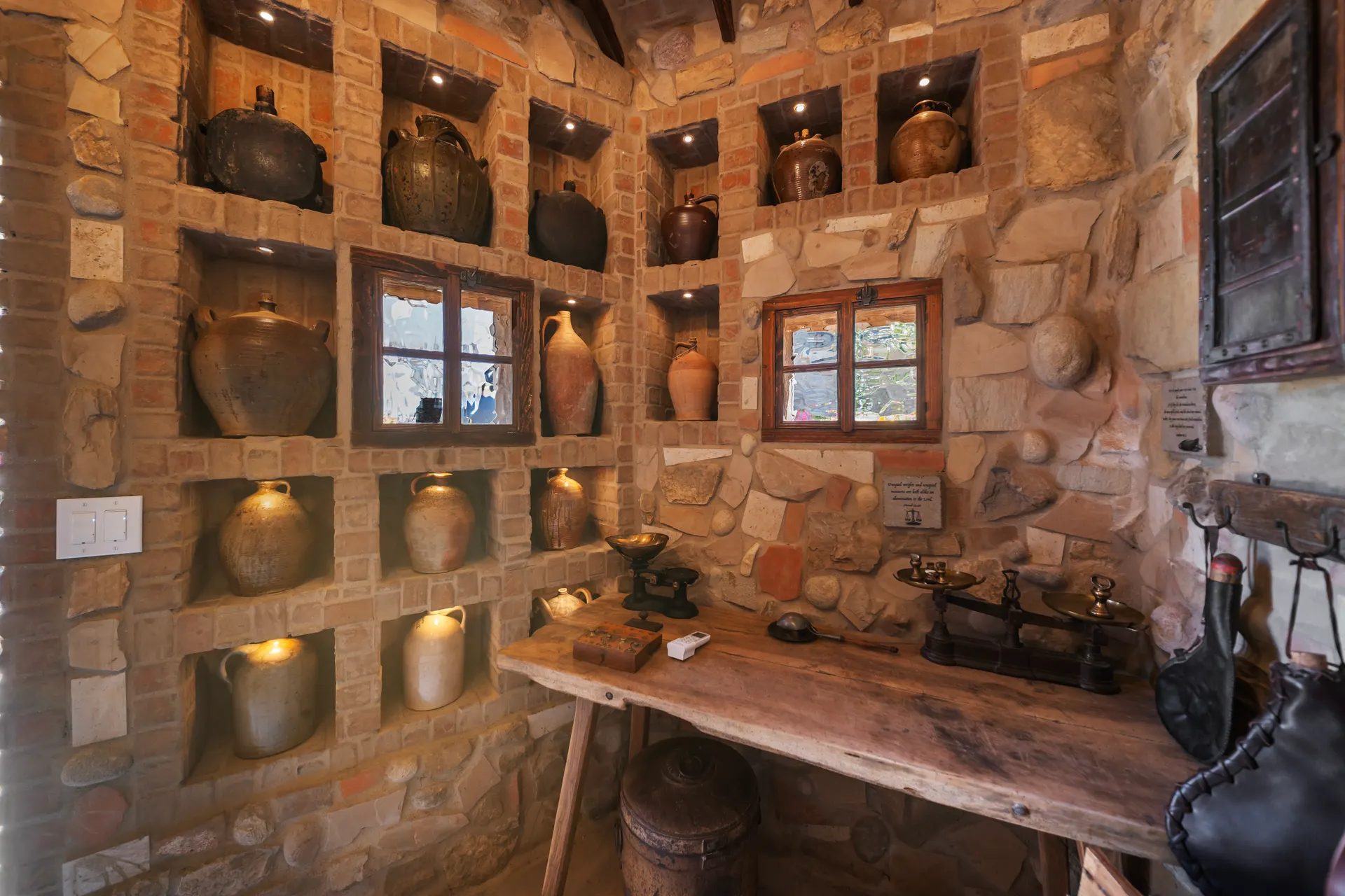 Amphorae set into lit niches in a stone wall above a timber table