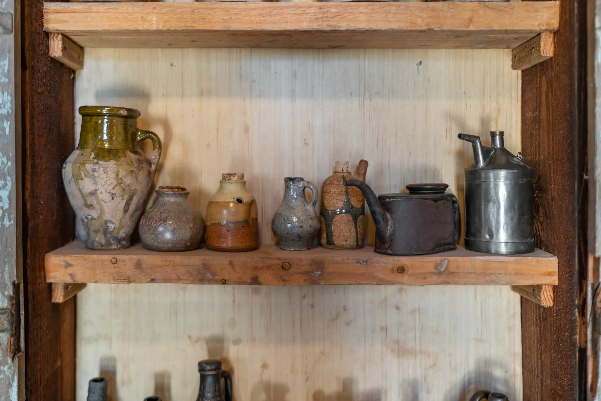 Shelf of glazed jugs and pewter vessels on rough timber